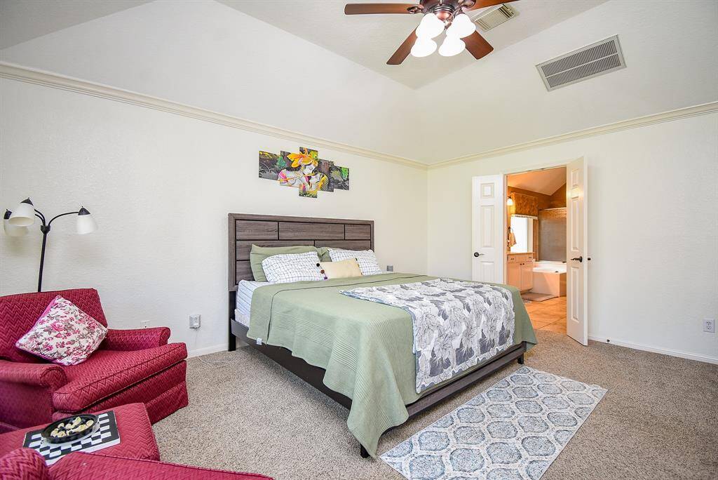 This spacious bedroom features a vaulted ceiling, a cozy seating area, and an en-suite bathroom. The neutral carpet and calming wall colors create a welcoming atmosphere.