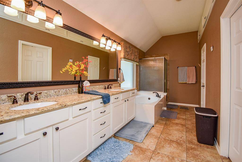 This bathroom features a spacious layout with a double vanity, granite countertops, and ample storage. It includes a large soaking tub and a separate shower, complemented by warm-toned walls and tile flooring.
