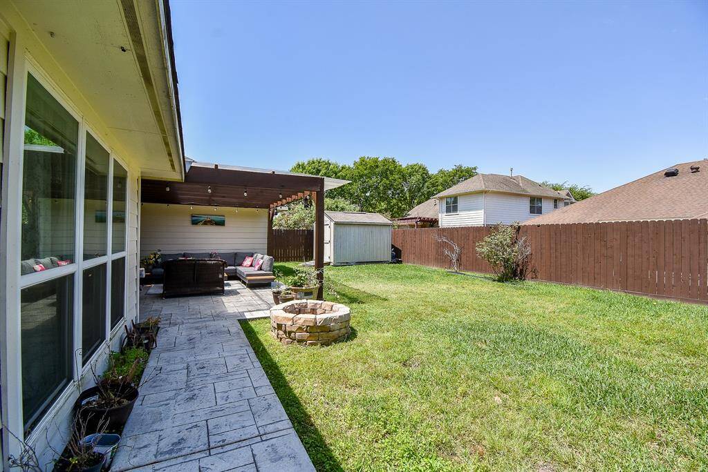 The yard is spacious with a well-maintained lawn, a small fire pit, and a storage shed. It's enclosed by a wooden fence, offering privacy and a cozy outdoor living space.