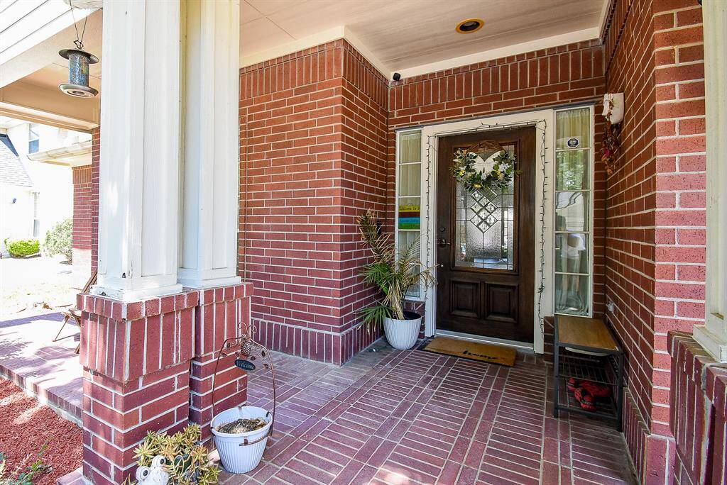 Charming brick front porch with a welcoming wooden door featuring decorative glass. The space can be accented with potted plants and bench seating, creating a cozy entrance.