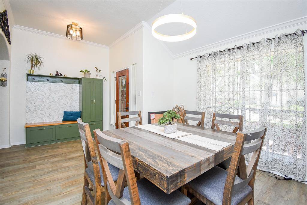 This dining area is brightened by large windows with sheer curtains, enhancing the inviting and airy ambiance. Modern light fixtures and tasteful decor add to the room's charm.