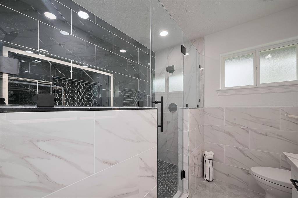 Tastefully renovated primary restroom with shower tile extending to the ceiling with a hexagon pattern on the floor and in the cut-out shelf