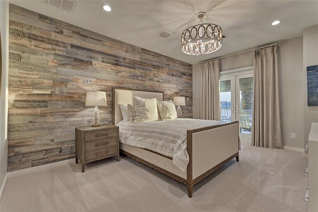 Guest bedroom #1 is a luxurious suite offering lake views and access to the outdoor balcony. Features include a rustic farmhouse feature wall, opulent lighting and plush carpeting.