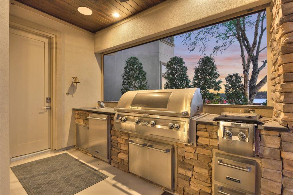 The outdoor kitchen includes top-of-the-line appliances including a Kitchen Aid Refrigerator, FireMagic Aurora Gas Grill & Dual Burner. Other amenities include a kitchen sink and double stainless-steel drawers.