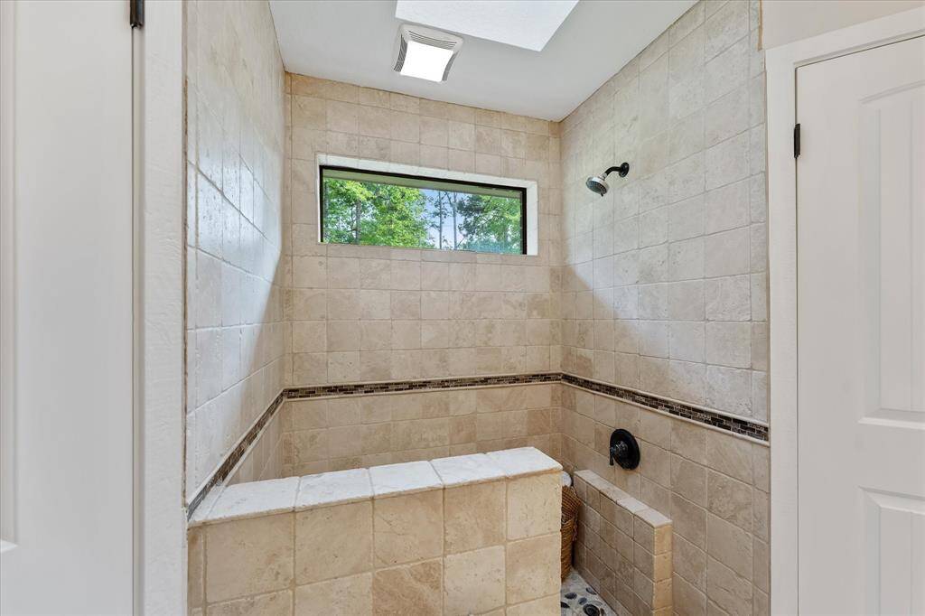 Experience natural light in the walk-in shower, featuring a window with a backyard view and a skylight.