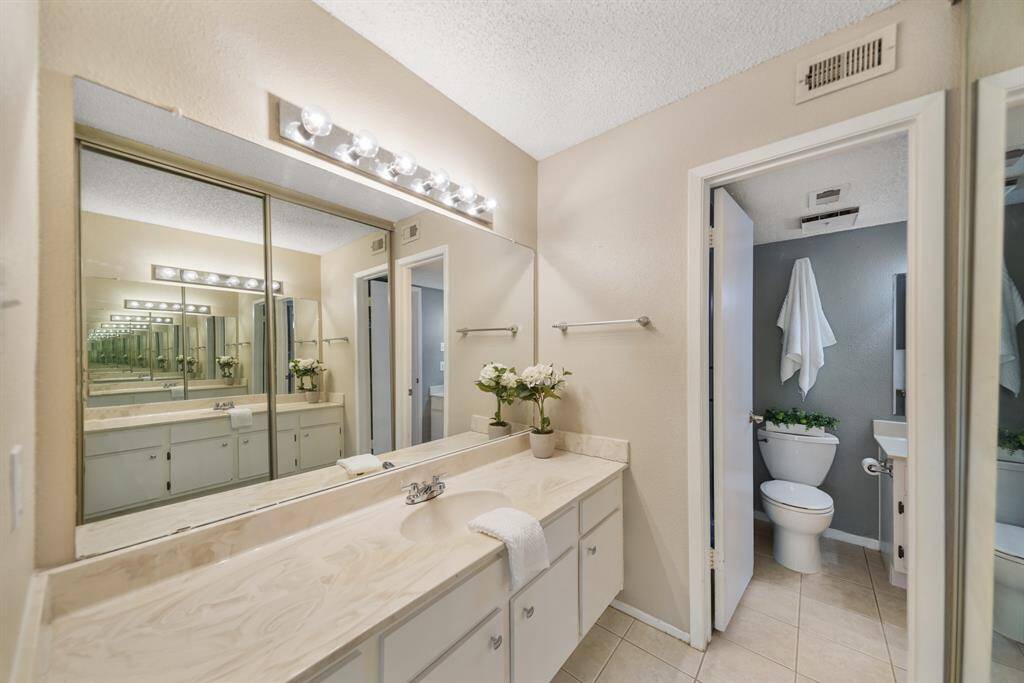 The private dressing area includes a large wall mounted mirror, plenty of counter, cabinet & drawer storage, full length wardrobe mirrors offering access to a large walk-in closet & tile flooring.