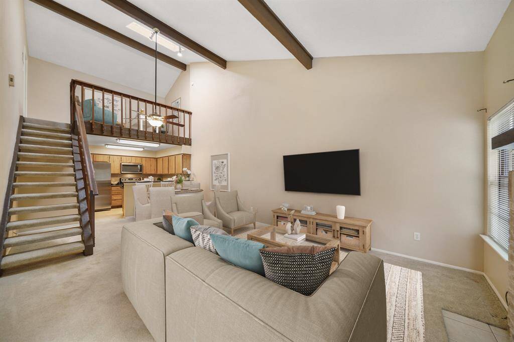 Absolutely beautiful, the living room boasts a high ceiling with wood-stained decorative beams and carpet. This photo has been virtually staged.