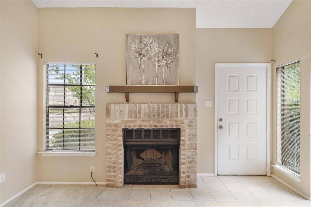 Cozy up to the brick surrounded wood burning fireplace with wood-stained mantel and tiled hearth sitting justnext to a large window with blinds overlooking the front yard.