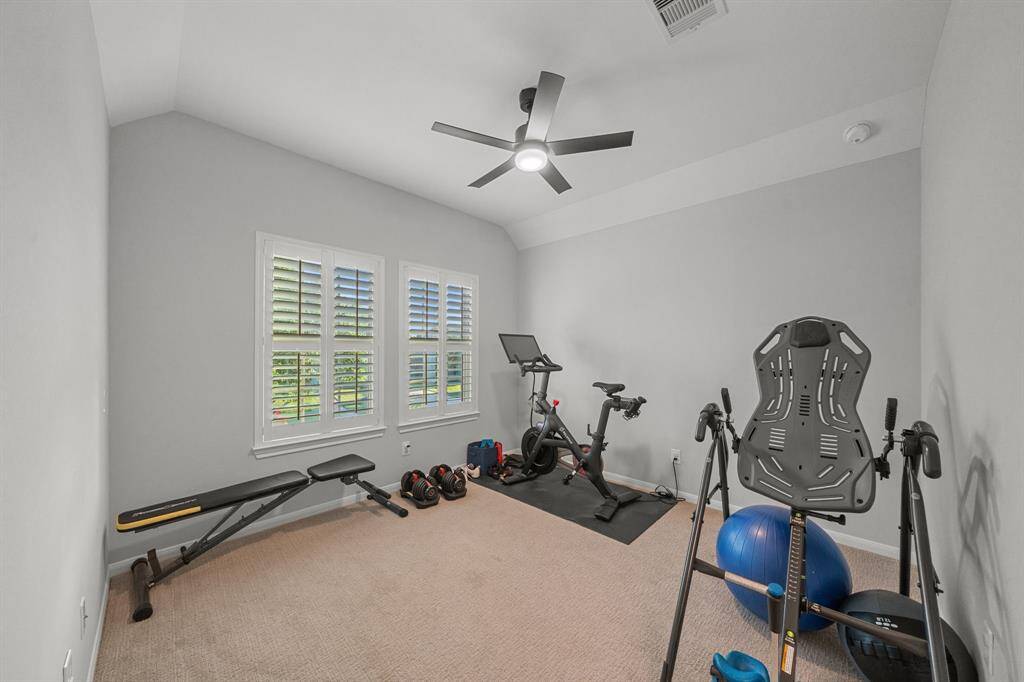 The spacious game room is carpeted and equipped with a ceiling fan, shades that allow for adjustable natural light. Included is a golf simulator, making it an ideal space for entertainment.