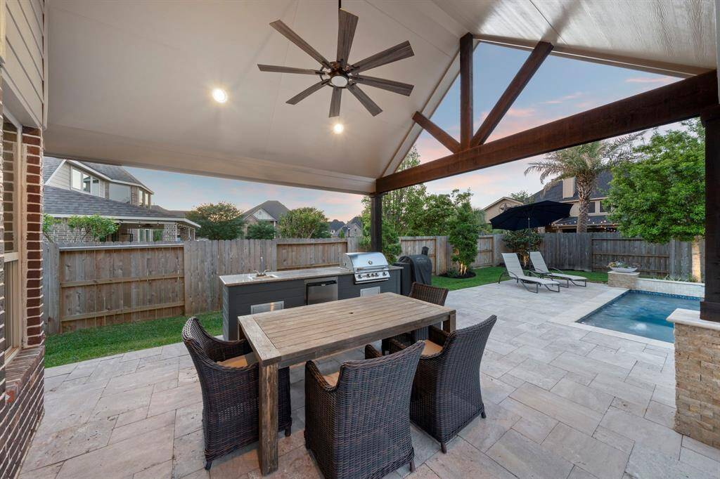 The outdoor kitchen area is fully equipped with a grill, sink, mini fridge, and a ceiling fan for comfort, complemented by a convenient pool bathroom addition.