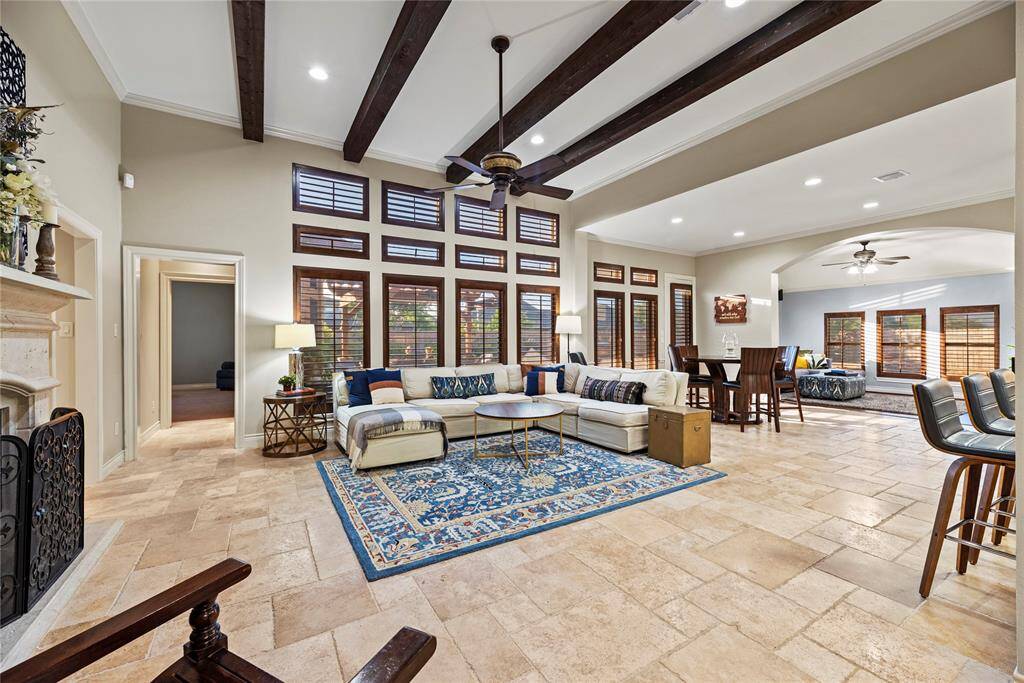 The expansive living area offers a perfect blend of comfort and sophistication, featuring striking exposed wood beams, elegant travertine flooring, and an abundance of windows that flood the space with natural light while offering stunning views of the picturesque backyard. Ideal for relaxing or entertaining in style.