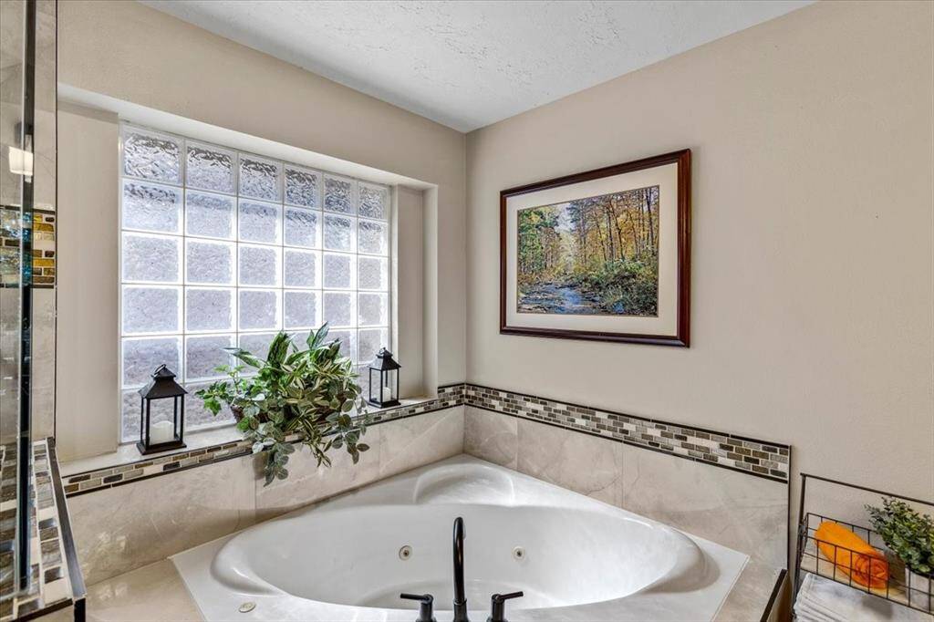The jetted soaking tub is a standout feature of the primary bathroom, surrounded by exquisite tile and enhanced by glass block accents that allow natural light to flood the space. This serene spot offers the perfect retreat for relaxation, combining luxury and comfort in a beautifully designed setting.