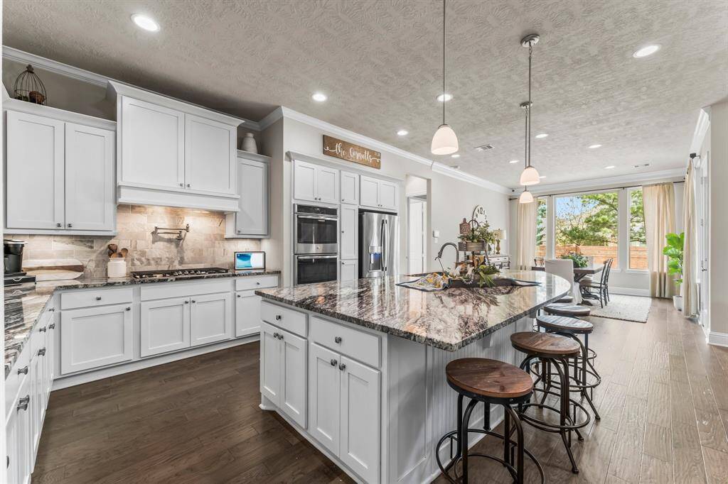 This stunning kitchen features white cabinetry, a large island with seating, and stainless steel appliances. It opens to a bright dining area with large windows overlooking the backyard.