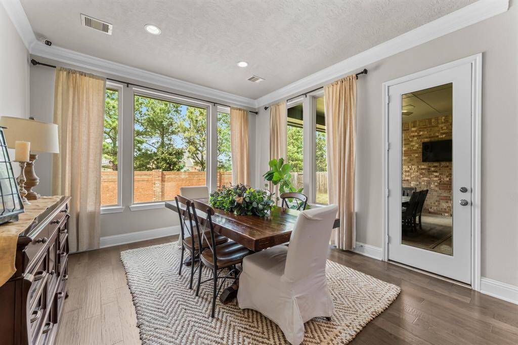 This bright and inviting dining room features large windows with a view of the backyard, hardwood floors, elegant crown molding, and access to a patio through a glass door.
