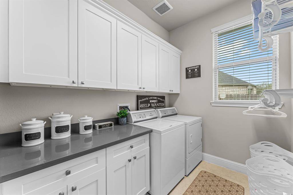 This is a bright, modern laundry room featuring white custom cabinetry, ample countertop space, and a window with natural light. It offers tons of storage and a clean, organized appearance.