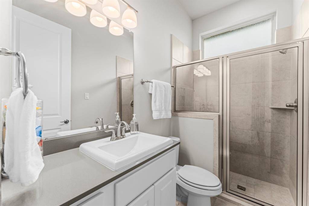 This ensuite bathroom features a sleek vanity with a square sink, a large mirror, and contemporary lighting. It includes a glass-enclosed shower with tiled walls and a frosted window for natural light.