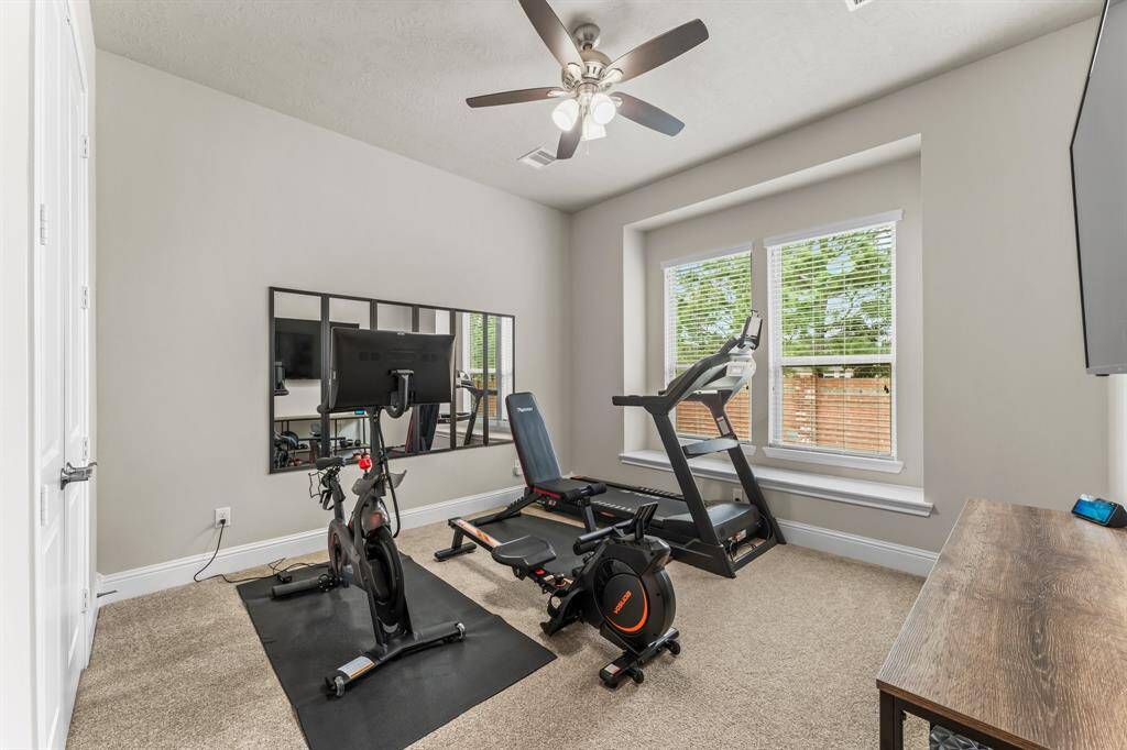 This is the secondary bedroom downstairs that is currently being used as a home gym. The room has large windows for natural light and a ceiling fan.