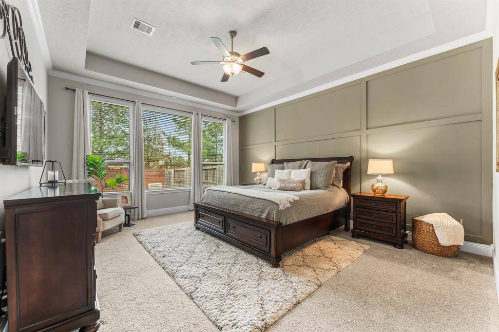 A true owner's retreat with large windows, a tray ceiling, ceiling fan, and elegant panel accent wall.