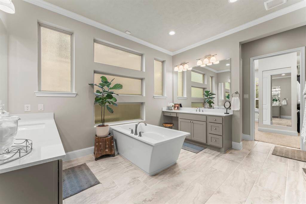 This modern bathroom features a freestanding bathtub, dual sinks with a large mirror, and ample natural light from multiple frosted windows. The neutral color palette and stylish lighting create a serene and elegant atmosphere.