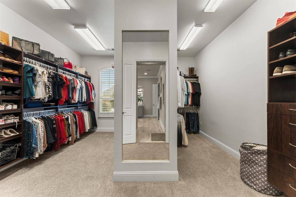 Spacious walk-in closet with ample storage, featuring built-in shelves, hanging space, a full-length mirror, and bright lighting.