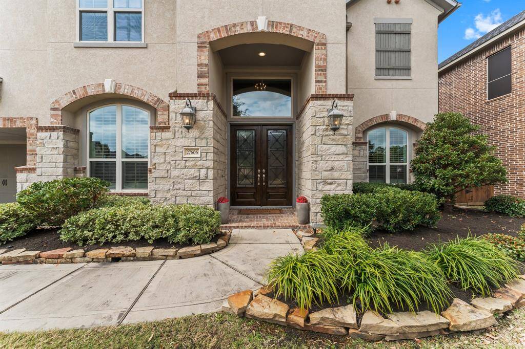 This photo showcases an elegant two-story home's entrance with a stone and brick facade. The arched windows and double doors enhance its curb appeal.