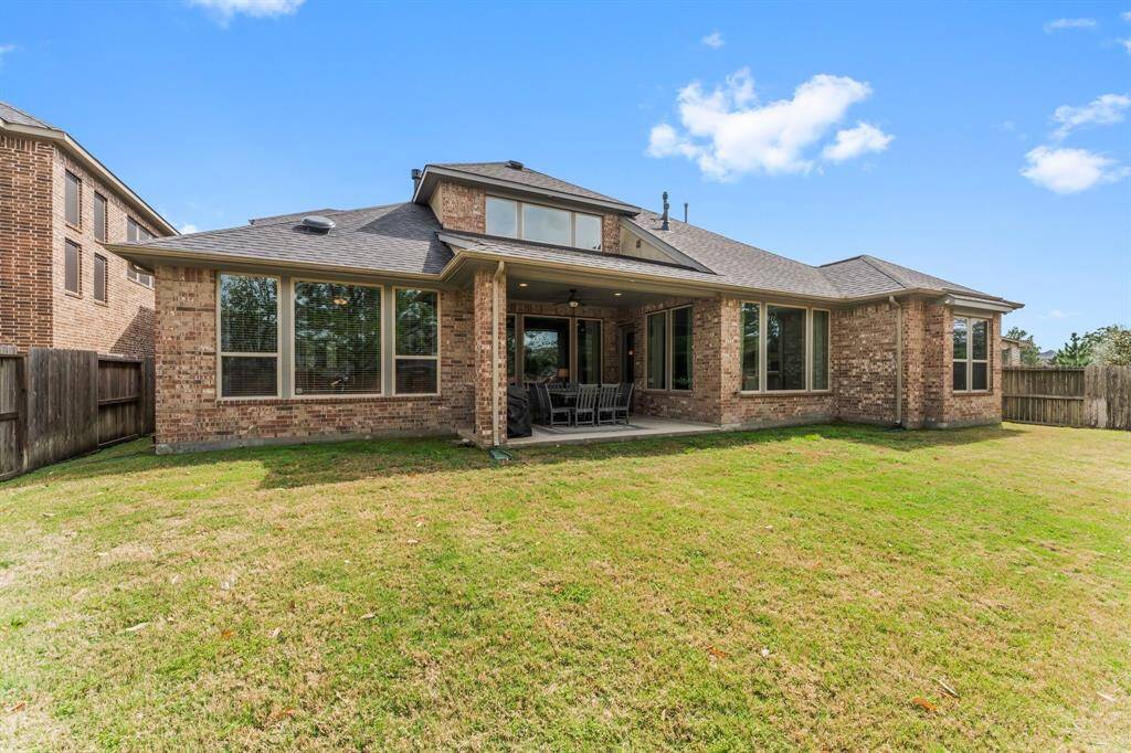 This photo showcases the spacious backyard, featuring a well-maintained lawn and a covered patio area, ideal for outdoor dining and relaxation. The large windows provide ample natural light to the interior.