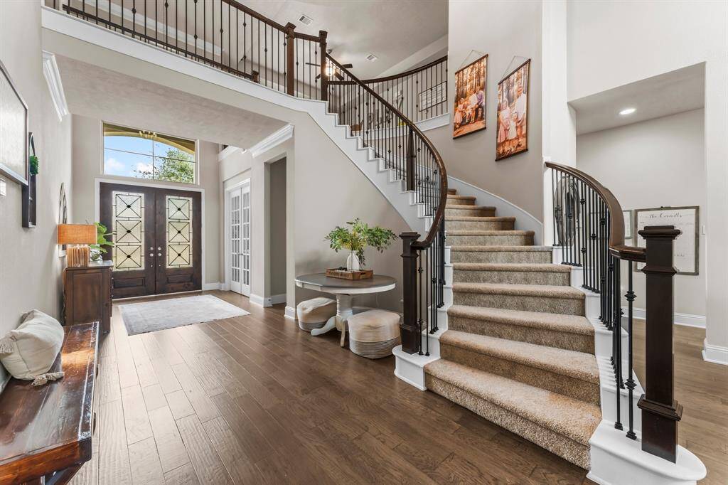 This elegant foyer features a grand, curved staircase with carpeted steps and wrought iron railings. The hardwood floors complement the neutral walls, creating a warm and inviting atmosphere.