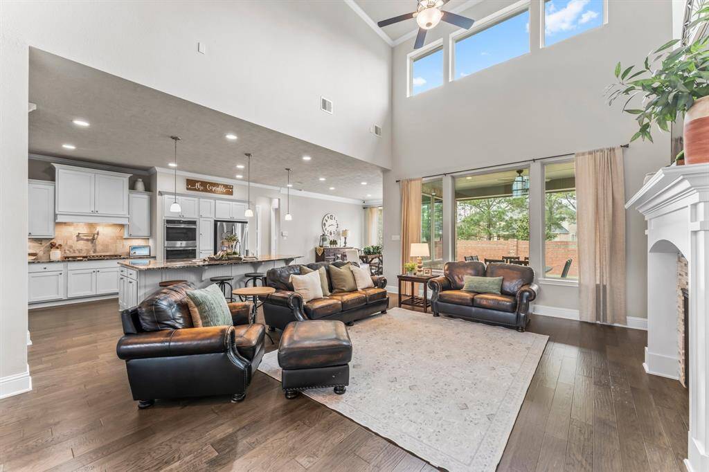 This spacious living area features high ceilings, large windows for natural light, and an open layout connecting to the kitchen. The room includes elegant hardwood floors and a cozy fireplace.