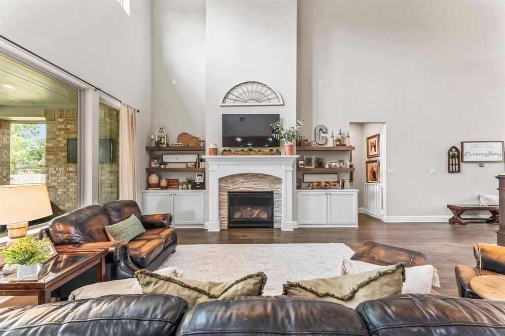 The living room features high ceilings, a cozy fireplace, and abundant natural light from large windows. It has elegant wood flooring, built-in shelves, and an open layout, perfect for comfortable living and entertaining.