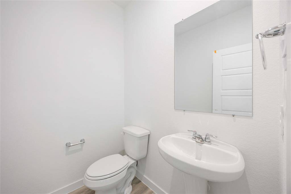 This half bath features a pedestal sink, toilet, and a large mirror. The room has a clean, minimalist design with white walls.