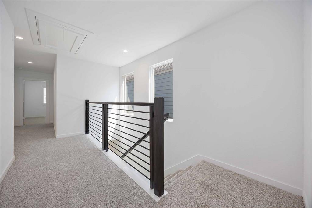 This photo showcases a bright, modern upstairs hallway with neutral carpet and sleek metal railing. Two windows provide natural light, enhancing the airy feel.