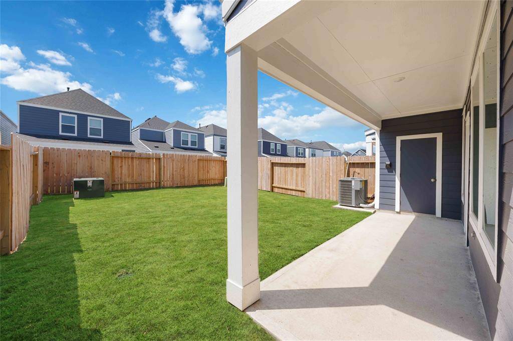 This photo shows a well-maintained backyard with a covered patio area, perfect for outdoor relaxation. The space is enclosed by a wooden fence, offering privacy. The yard features a lush green lawn and is located in a neighborhood with similar homes nearby.