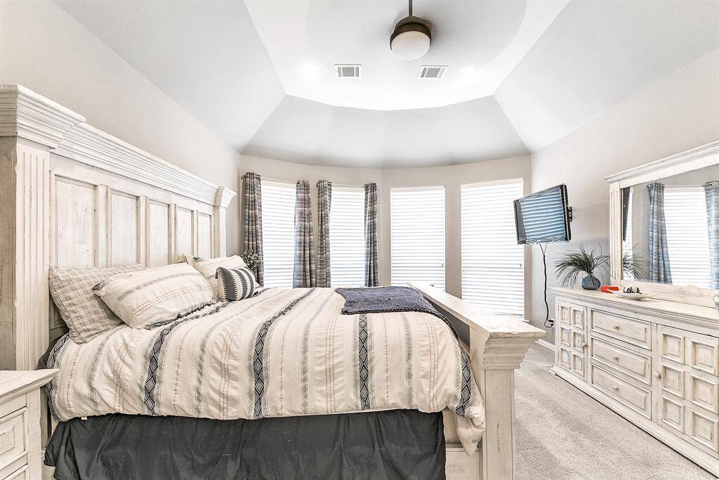 This first-floor primary suite offers the ultimate in privacy and comfort, with its own private entrance off the living room hall. The room features a tray ceiling, plush carpeting, and four large windows that frame serene views of the backyard. With ample space, this bedroom is the perfect retreat for unwinding after a long day.