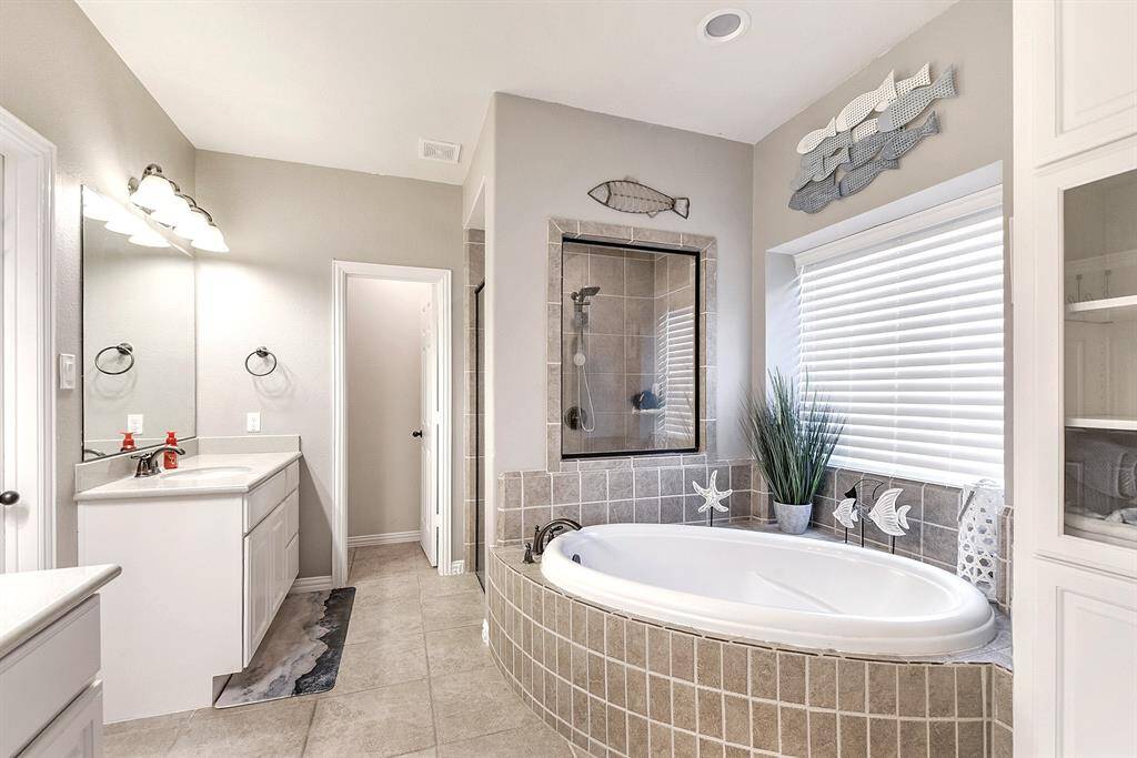 This elegant master bathroom is designed for relaxation and convenience, featuring a soaking bathtub, a separate standing shower, and separate sinks and vanities. The space is enhanced by white cabinetry, oil-rubbed bronze fixtures, and a walk-in closet for all your storage needs. Enjoy added privacy with a separate toilet area and the convenience of extra built-ins for organization.