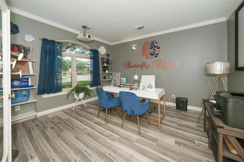 This photo showcases a stylish home office with gray walls, wood flooring, and a large window with blue curtains. It features a modern white desk, blue chairs, and tasteful decor, creating a bright and inviting workspace.