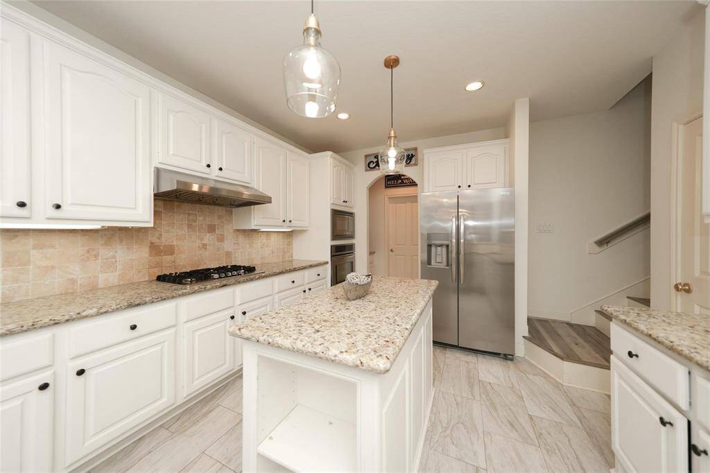 Bright kitchen with modern stainless steel appliances, granite countertops, white cabinetry, and a central island. It features a gas stove and tiled backsplash, creating a clean and functional space.