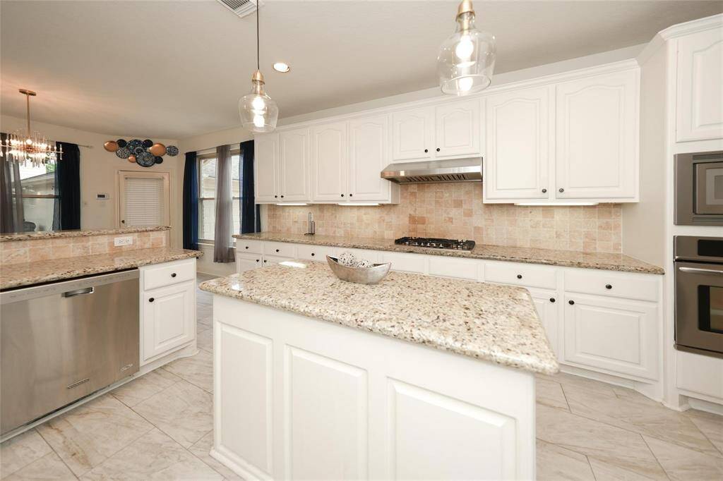 This kitchen features elegant white cabinetry, granite countertops, and stainless steel appliances. It includes a spacious island, modern lighting fixtures, and a cozy breakfast nook with large windows.