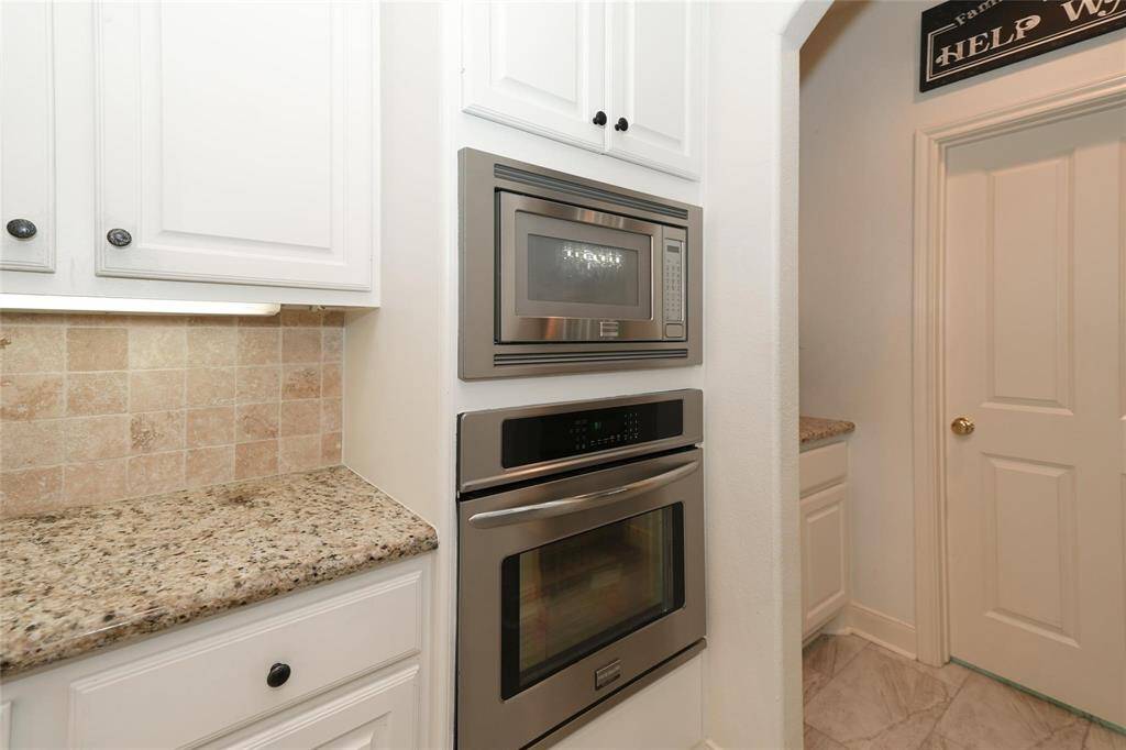 This kitchen features modern stainless steel appliances, including a built-in microwave and oven. It has granite countertops and white cabinetry, offering a clean and elegant look.