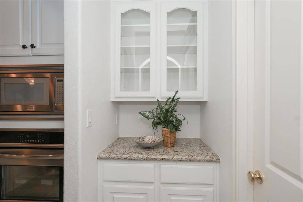 This photo showcases a compact kitchen nook with granite countertops, white cabinetry, and built-in appliances. The display cabinet adds a touch of elegance, perfect for showcasing decor or dishware.
