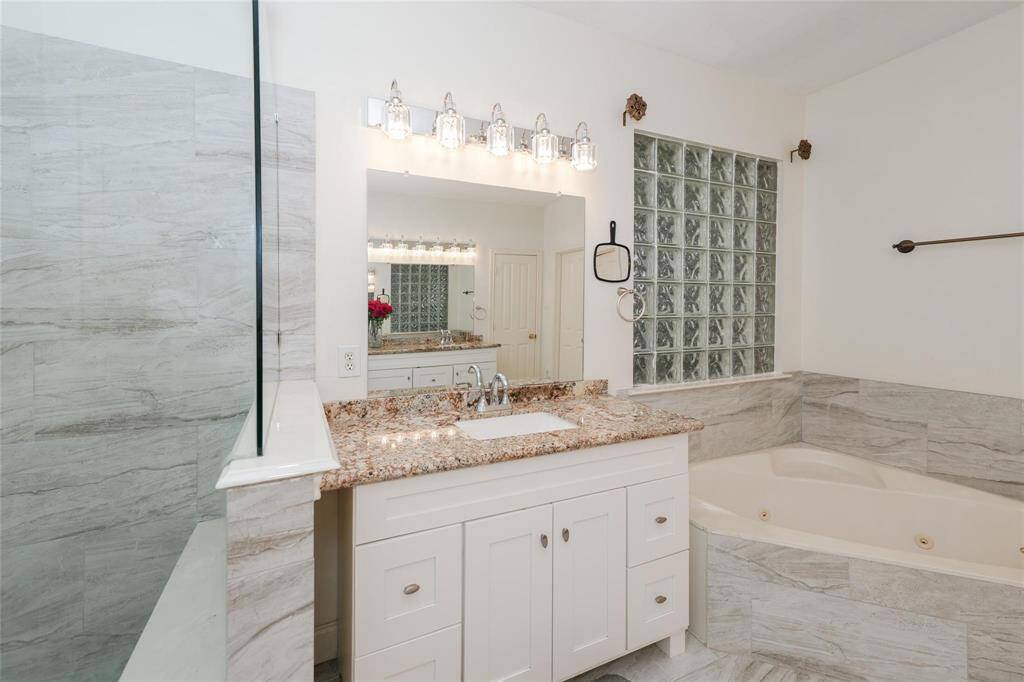 This bathroom features a modern design with a granite countertop, under-mount sink, and a spacious tub. It has a large mirror, elegant lighting, and a glass block accent wall, creating a bright and inviting space.