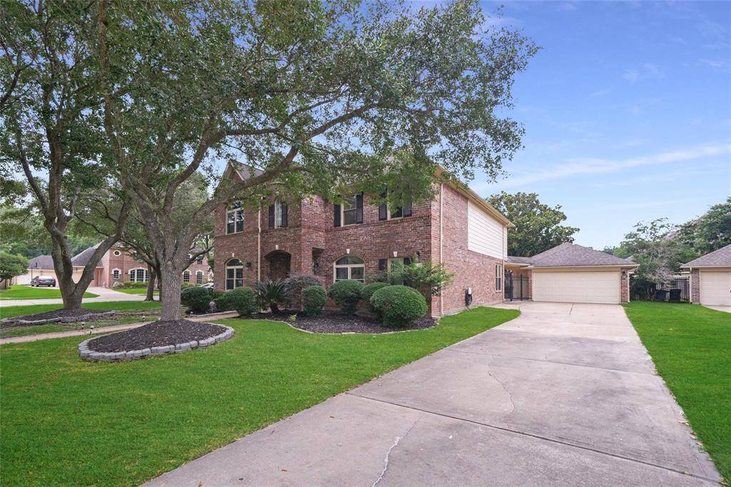 This photo features a two-story brick house with a spacious driveway leading to a detached garage. The well-maintained front yard includes mature trees and landscaped bushes, offering a welcoming and serene environment.