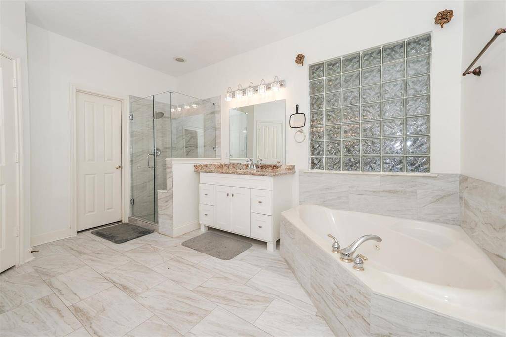 This spacious bathroom features a large soaking tub, a glass-enclosed shower, and a modern vanity with dual sinks. The room is accented with elegant tile flooring and a frosted glass window for natural light and privacy.