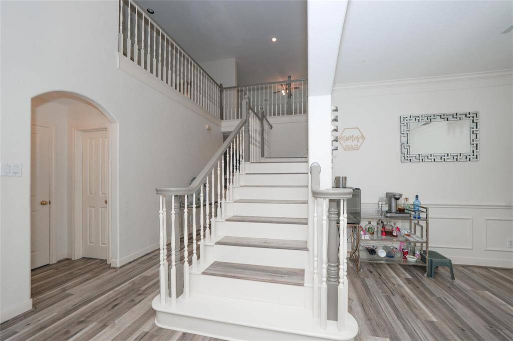 This photo showcases a spacious, modern entryway with light wood flooring and a prominent staircase leading to an upper level. The area features elegant white walls with decorative molding and ample natural light. A bar cart adds a touch of functionality and style.