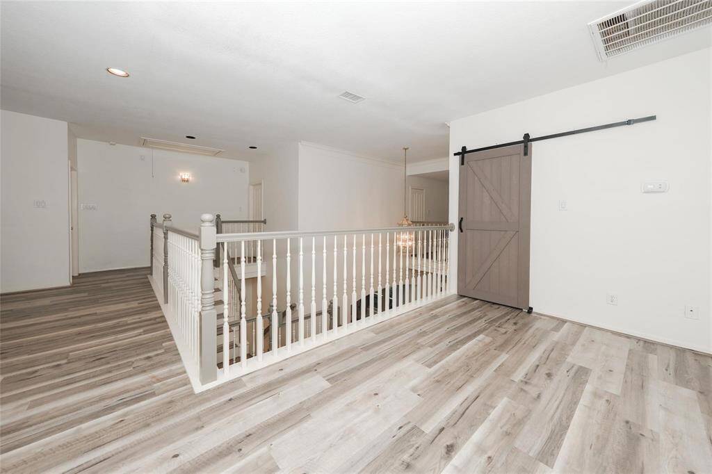 This bright and spacious area features modern laminate flooring, an open staircase with a white railing, and a stylish sliding barn door, creating a welcoming and contemporary upper-level space.