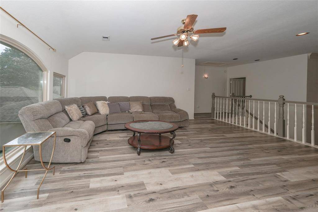 This spacious living area features a large sectional sofa, a ceiling fan, and stylish wood flooring. An arched window provides natural light, complementing the open layout with a view of the staircase railing.