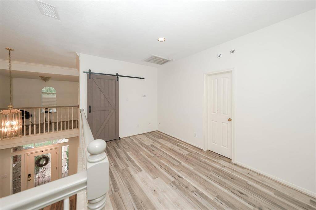 This photo shows a bright, open space with light wood flooring and neutral walls. It features a sliding barn door and overlooks an entryway with a decorative glass front door. Perfect for a cozy sitting area or small office.