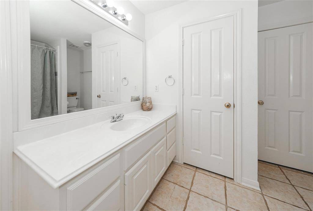 Bright bathroom with a large mirror, single sink vanity, and ample cabinet storage. Features tiled floors and a separate shower area with a curtain.