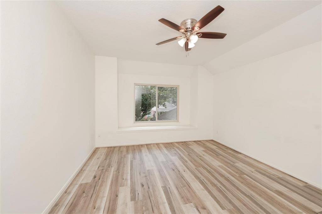 This room features clean white walls, wood-look flooring, and a ceiling fan with lights. A large window provides natural light and a view of the outdoors, making the space bright and inviting.