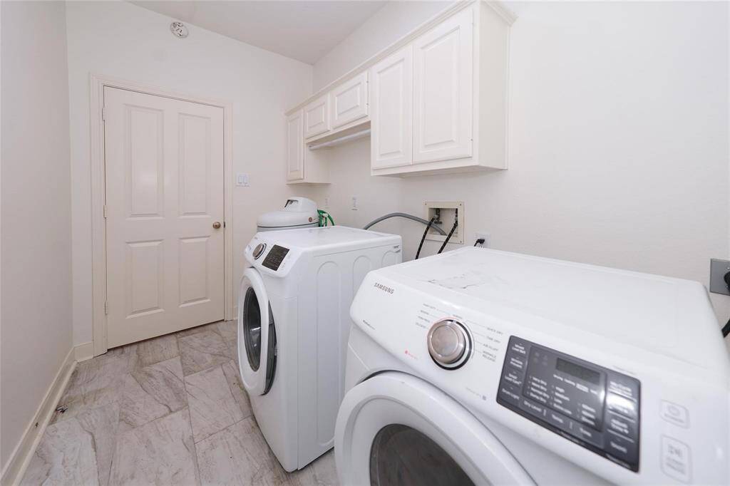 This photo features a clean, well-lit laundry room with modern appliances, including a washer and dryer. It has white cabinets for storage and a tiled floor, providing a practical and functional space.