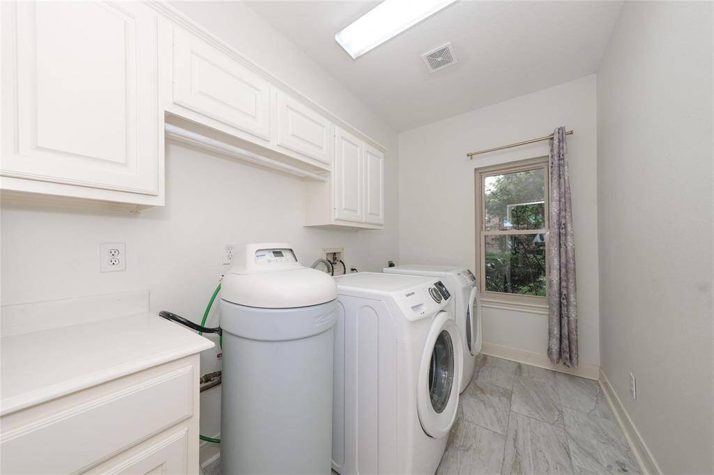 This photo shows a bright laundry room with modern appliances, ample cabinetry for storage, and a window for natural light. The space has a clean, functional design and tiled flooring.